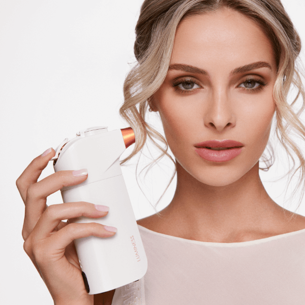 Close up photo of a woman holding the airbrush skincare device next to her face