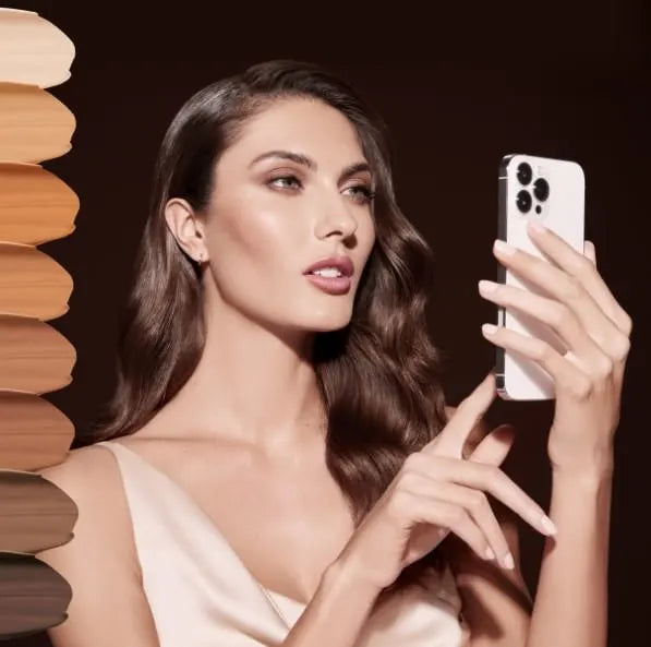 Female model holding up a photo as she looks at it. On left side of image, there are multiple foundation color swatches bleeding off the image