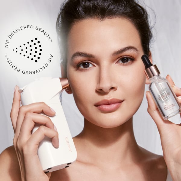 Woman posing with a skincare device in one hand and bottle of serum in another. An overlay graphic in the left hand corner reads 