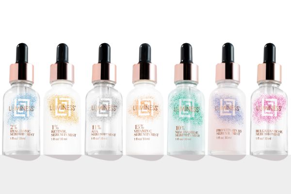 Product shot of seven bottles of skincare serum lined up from left to right of image.